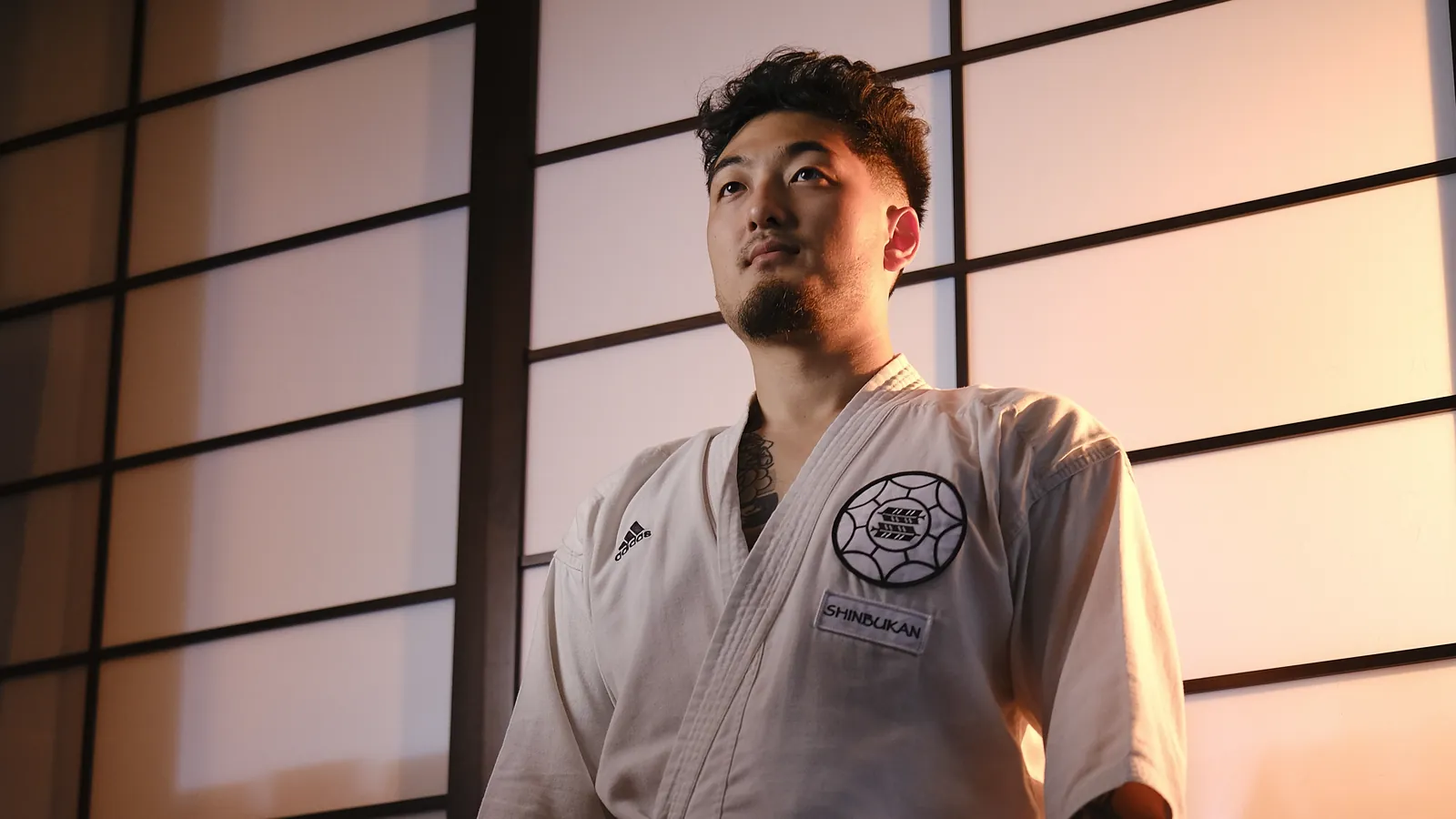 Harrison Saito in his gi and black belt, standing before a lit shoji screen at the Shinbukan dojo