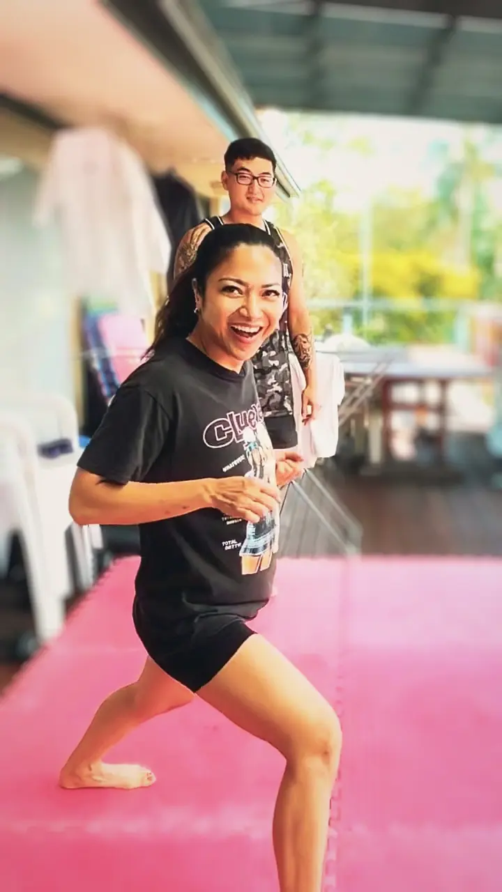 A student mid-drill on the mats, laughing, Harrison behind her