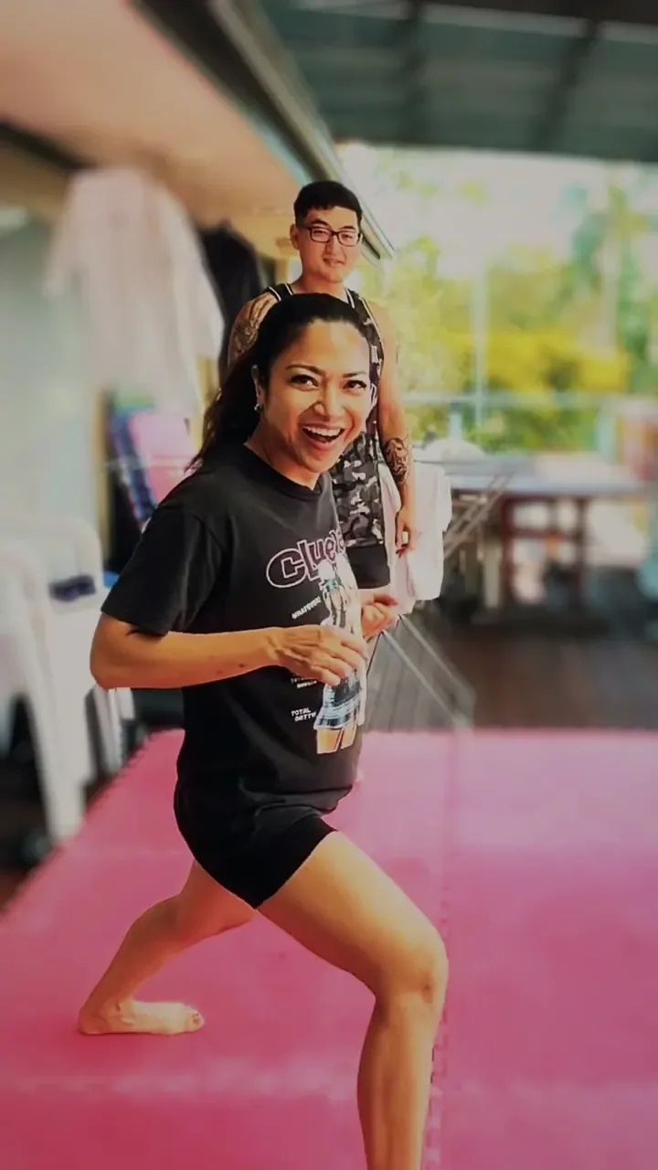 A student mid-drill on the mats, laughing, Harrison behind her