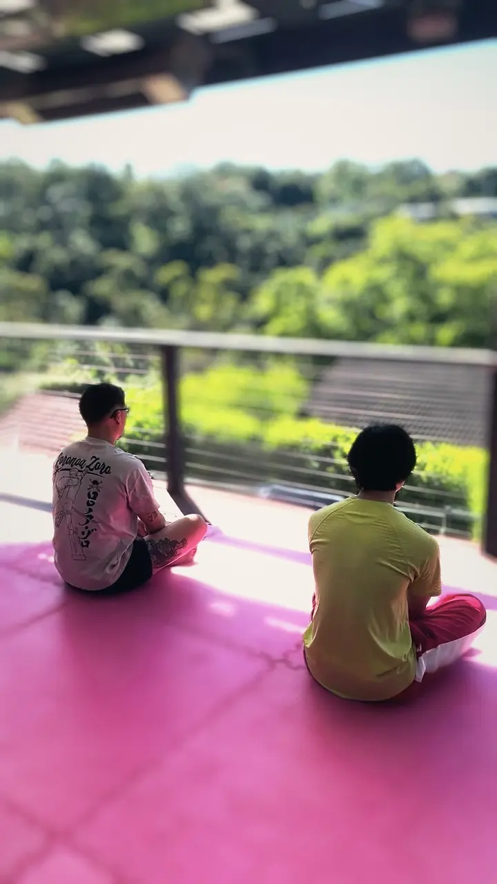 Harrison and a student sitting on the mats, seen from behind, looking out over the valley