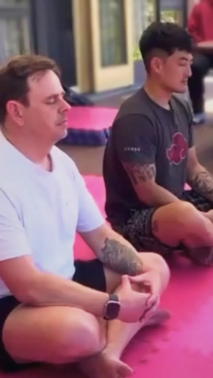 Harrison and a client sitting cross-legged in meditation on the mats
