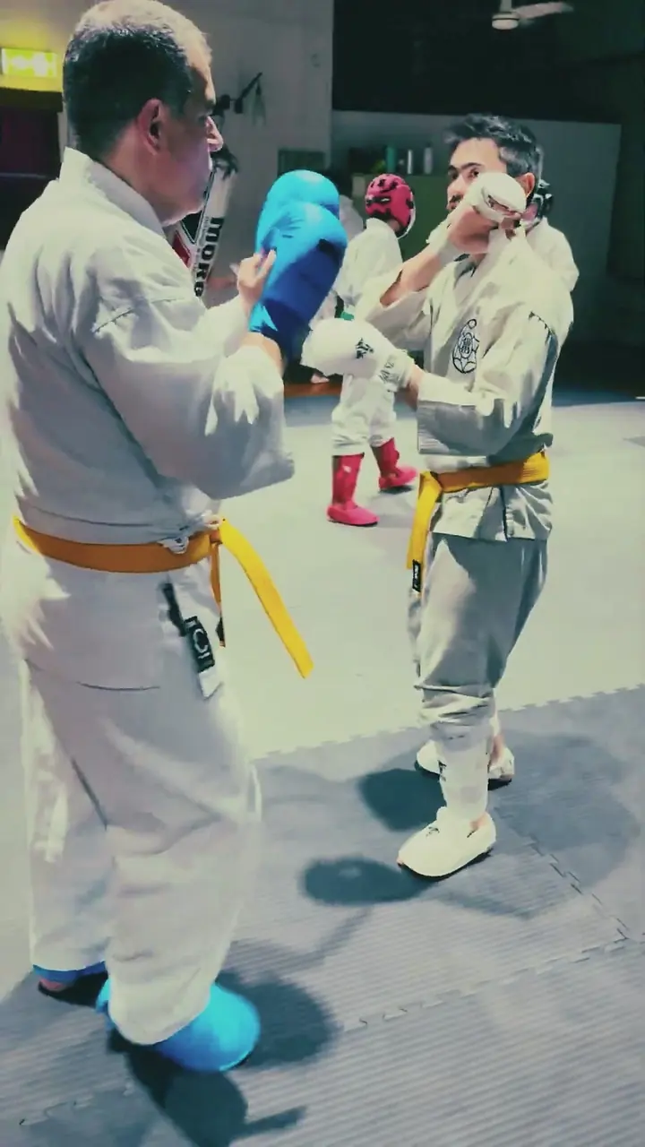 Two karateka in gi and gloves sparring in the dojo
