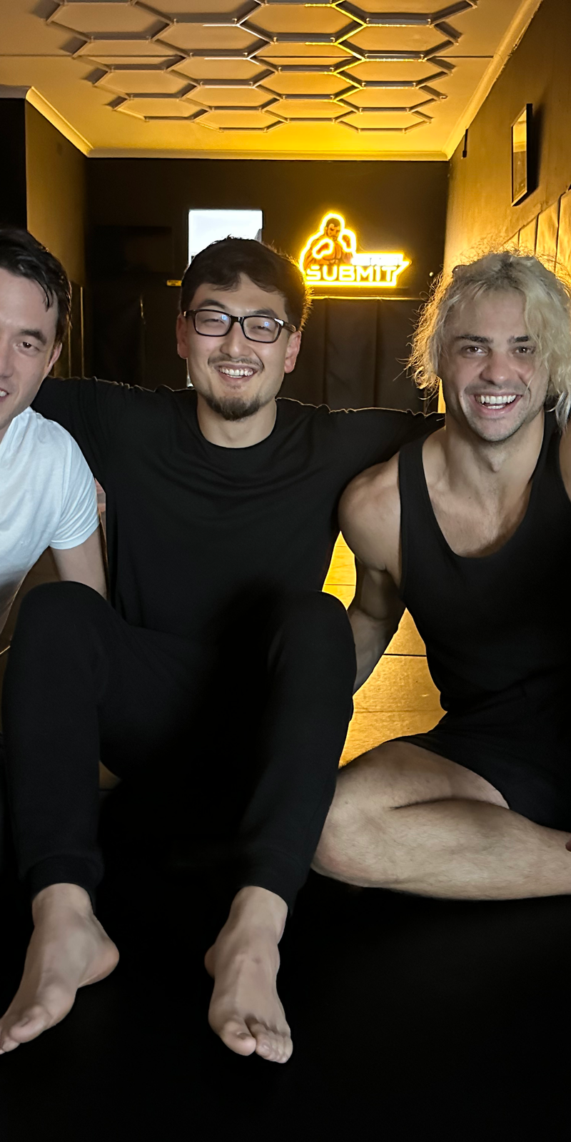 Harrison seated on black mats with Andrew Koji and Noah Centineo